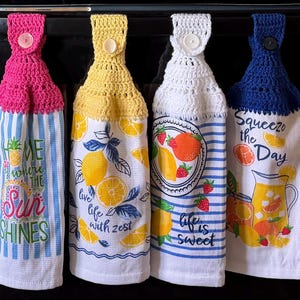 May include: Four hanging kitchen towels with crochet tops and button closures. The towels feature various designs, including lemons, strawberries, and the phrases "Home Where the Sun Shines", "Live Life with Zest", "Life is Sweet", and "Squeeze the Day".