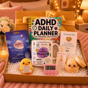 May include: A gift box containing a planner, mug, face mask, and timer. The planner reads "ADHD DAILY PLANNER". The mug says "the Morning Mindset mug". Other items include a "Positive Donut" and a "Positive Duck". The box is filled with shredded paper.