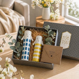 May include: A gift set containing two ceramic figures, one white with blue detailing, the other yellow and white striped. The figures are presented in a box with decorative paper and greenery, with a card that says "Especially for you."