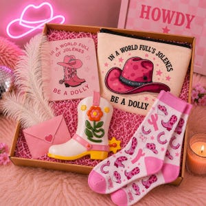 May include: A gift box containing a pink notebook, a beige zippered pouch, a white cowboy boot-shaped container with a flower design, a pink envelope with a heart, and white socks with pink cowboy boot and horseshoe patterns, all featuring the text IN A WORLD FULL'S JOLENES BE A DOLLY.