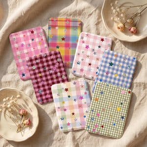 May include: A collection of six rectangular pocket mirrors featuring various gingham plaid patterns in pink, dark red, rainbow, light pink, blue, and olive green, all decorated with small, scattered, holographic star-shaped stickers.