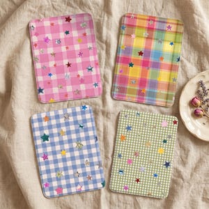 Puede incluir: Cuatro posavasos rectangulares con esquinas redondeadas, cada uno con un patrón de cuadros o vichy distinto en rosa, multicolor, azul o verde, decorado con pegatinas reflectantes en forma de estrella holográfica.