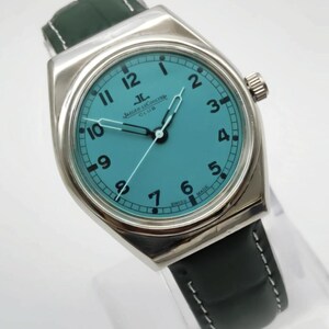 Pode incluir: Um rel&oacute;gio de pulso prateado com mostrador turquesa e algarismos pretos. O rel&oacute;gio apresenta uma bracelete de couro preta com pespontos brancos. O mostrador exibe o log&oacute;tipo Jaeger LeCoultre Club. Um acess&oacute;rio elegante.