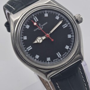 Puede incluir: Un reloj de pulsera de acero inoxidable con esfera negra y correa de cuero negra. El reloj presenta marcadores de hora blancos, un segundero rojo y el texto "ULYSSES NARDIN SWISS MADE". Tiene un bisel plateado y una correa de cuero negro texturizado.