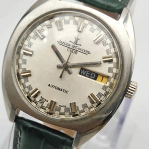 Puede incluir: Un reloj de pulsera autom&aacute;tico Jaeger-LeCoultre Club plateado con esfera blanca y correa de cuero verde. La esfera muestra el d&iacute;a de la semana. El reloj tiene agujas e indicadores plateados. Dise&ntilde;o cl&aacute;sico.