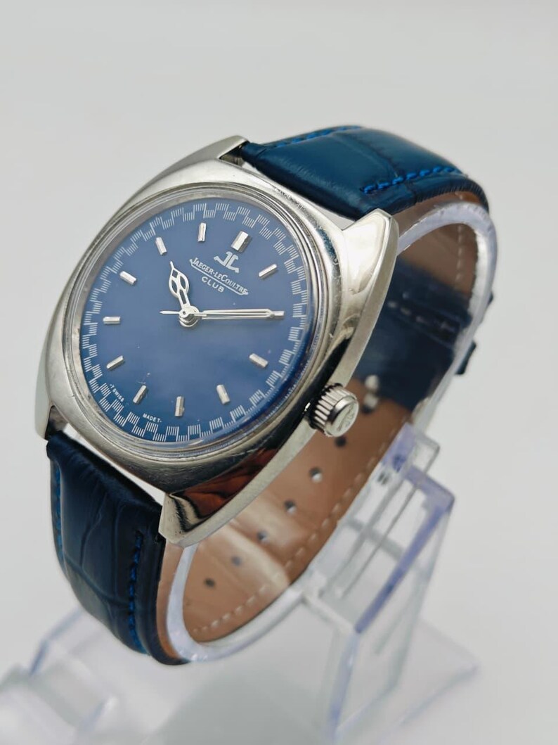 Puede incluir: Un reloj Jaeger-LeCoultre Club vintage con esfera azul y caja plateada. El reloj tiene una correa de cuero azul. La esfera muestra el logotipo de Jaeger-LeCoultre y la palabra "CLUB".