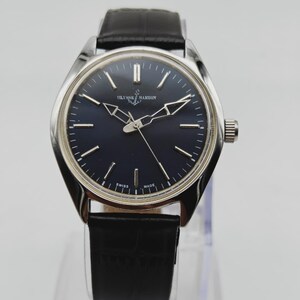 May include: A silver-toned Ulysse Nardin wristwatch with a dark blue face and black leather band. The watch features a round face with silver hands and markers. The text "SWISS MADE" is visible on the watch face.