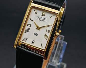 Orologio da polso vintage Seiko Slim Tank al quarzo con quadrante bianco, cassa rettangolare dorata e cinturino nero.