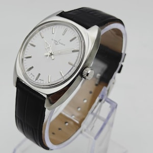 May include: A silver-toned wristwatch with a white face and black leather band. The watch features silver hands and hour markers. The band has a textured, crocodile-like pattern. The watch is displayed on a clear stand.