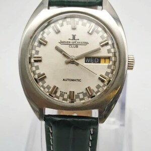 Puede incluir: Un reloj Jaeger-LeCoultre Club vintage con caja plateada y esfera blanca. El reloj presenta una pantalla de d&iacute;a y fecha y una correa de cuero verde. La esfera muestra el texto "AUTOMATIC" y "SWISS MADE".