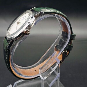 Pu&ograve; includere: Un orologio da polso argentato con quadrante bianco e cinturino in pelle verde. L'orologio ha un quadrante rotondo con lancette e indici argentati. Il cinturino verde &egrave; strutturato e ha una chiusura a fibbia. L'orologio &egrave; esposto su un supporto trasparente.