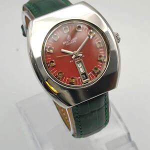 May include: A vintage Breitling Geneve automatic watch with a red dial and silver-tone case. The watch features a date display and is set on a green leather strap. The watch has a rectangular face.