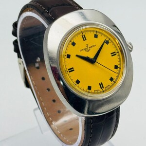 May include: A vintage Ulysse Nardin wristwatch with a bright yellow face and black markers. The watch has a silver-tone case and a dark brown leather strap. The watch face displays the brand name and an anchor logo.