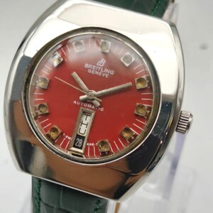 May include: A vintage Breitling Geneve automatic watch with a red dial and a green leather strap. The watch has a silver-colored case and a date display at the 6 o'clock position. The watch face has gold-colored hour markers.