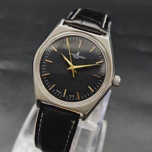 May include: A Ulysse Nardin wristwatch featuring a round black dial with gold-toned hour markers and hands. The watch has a silver-toned stainless steel case and a black leather strap with white stitching. The text Ulysse Nardin is printed on the dial.