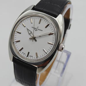 May include: A silver-toned wristwatch with a white face and black leather band. The watch face features the brand name "Ulysse Nardin" and the words "Swiss Made". The watch has a classic design.