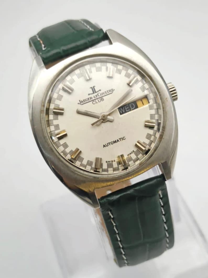 Puede incluir: Reloj autom&aacute;tico Jaeger-LeCoultre Club plateado con esfera blanca y correa de cuero verde. La esfera muestra el d&iacute;a de la semana y las palabras "AUTOMATIC" y "SWISS MADE".