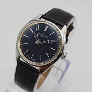 May include: A silver-toned Ulysse Nardin wristwatch with a dark blue face and black leather band. The watch features silver hands and markers, and the words "Ulysse Nardin" are printed on the face. The band has a crocodile pattern.