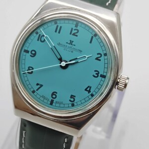 Pode incluir: Um rel&oacute;gio prateado com mostrador turquesa e algarismos pretos. O rel&oacute;gio apresenta o texto "JAEGER LECOULTRE CLUB" e tem uma bracelete em pele verde escura. Os ponteiros do rel&oacute;gio s&atilde;o prateados. O rel&oacute;gio &eacute; um rel&oacute;gio cl&aacute;ssico.
