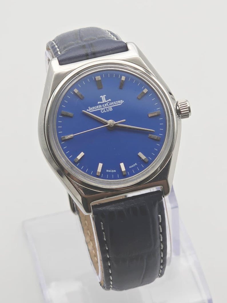 May include: A stainless steel Jaeger-LeCoultre Club watch with a blue dial and black leather strap. The watch features silver hour markers and hands. The dial has the Jaeger-LeCoultre logo and the word "CLUB" printed on it. The watch is marked "SWISS MADE".