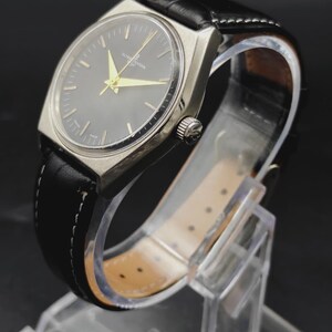 May include: A wristwatch with a silver-toned case and a round black dial featuring gold-colored hands and hour markers. The watch is attached to a black leather strap with white stitching and a silver crown on the side of the case.