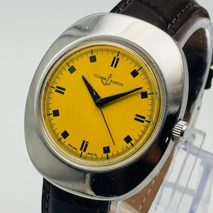 May include: A vintage Ulysse Nardin wristwatch with a bright yellow face and black markers. The watch has a silver-tone case and a dark brown leather strap. The watch face displays the brand name and the words "SWISS MADE".