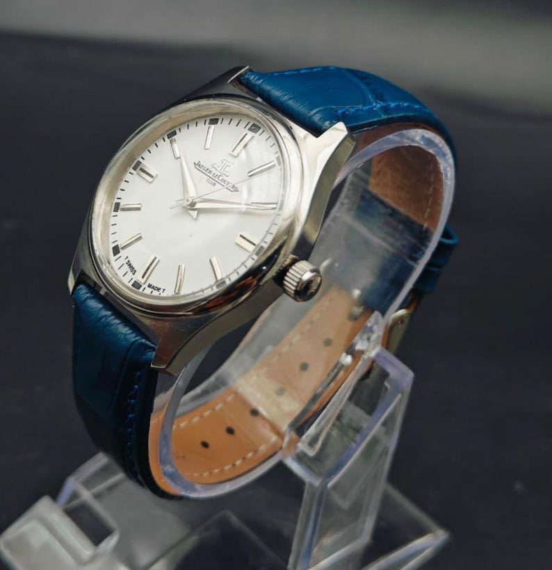 Peut inclure: Une montre-bracelet argent&eacute;e avec un cadran blanc et un bracelet en cuir bleu. La montre a un cadran rond avec des aiguilles et des marqueurs argent&eacute;s. Le bracelet bleu est textur&eacute; et poss&egrave;de une boucle. La montre est expos&eacute;e sur un pr&eacute;sentoir transparent.