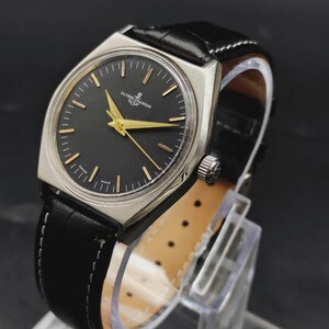 May include: A Ulysse Nardin wristwatch with a black dial, gold-tone hands, and gold-tone hour markers. The watch features a silver-tone metal case and a black leather strap with white stitching. The text Ulysse Nardin is printed on the dial.
