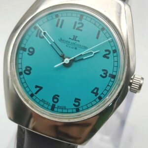 Op de afbeelding: Een vintage Jaeger-LeCoultre Club horloge met een turquoise wijzerplaat en een zilverkleurige kast. Het horloge heeft zwarte cijfers, witte wijzers en een bruine leren band. De tekst "JAEGER-LECOULTRE CLUB" is zichtbaar. Swiss Made.
