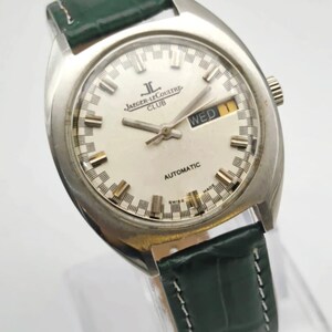 Puede incluir: Reloj autom&aacute;tico Jaeger-LeCoultre Club plateado con esfera blanca y correa de cuero verde. La esfera muestra el d&iacute;a de la semana y las palabras "AUTOMATIC" y "SWISS MADE".