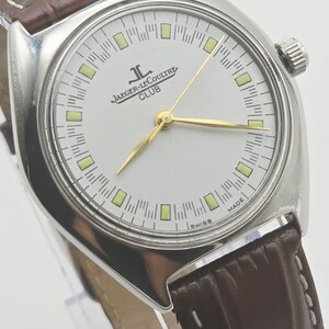 May include: A silver-toned Jaeger-LeCoultre Club watch with a white face, gold hands, and a brown leather band. The watch face features the Jaeger-LeCoultre logo and the word "CLUB". The watch has a round face and a textured brown leather band.