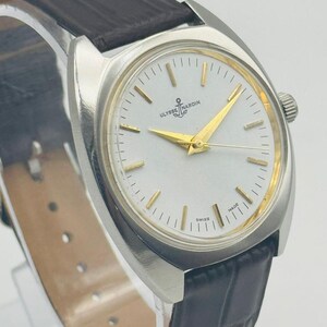 May include: A silver wristwatch with a white face and gold hands. The watch has a black leather strap and the brand name "Ulysse Nardin" on the face. The watch is a classic design.