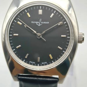 Puede incluir: Un reloj de pulsera Ulysse Nardin plateado con esfera negra y correa de cuero negro. La esfera del reloj tiene marcadores y agujas plateadas y doradas. El reloj est&aacute; marcado "Swiss Made".