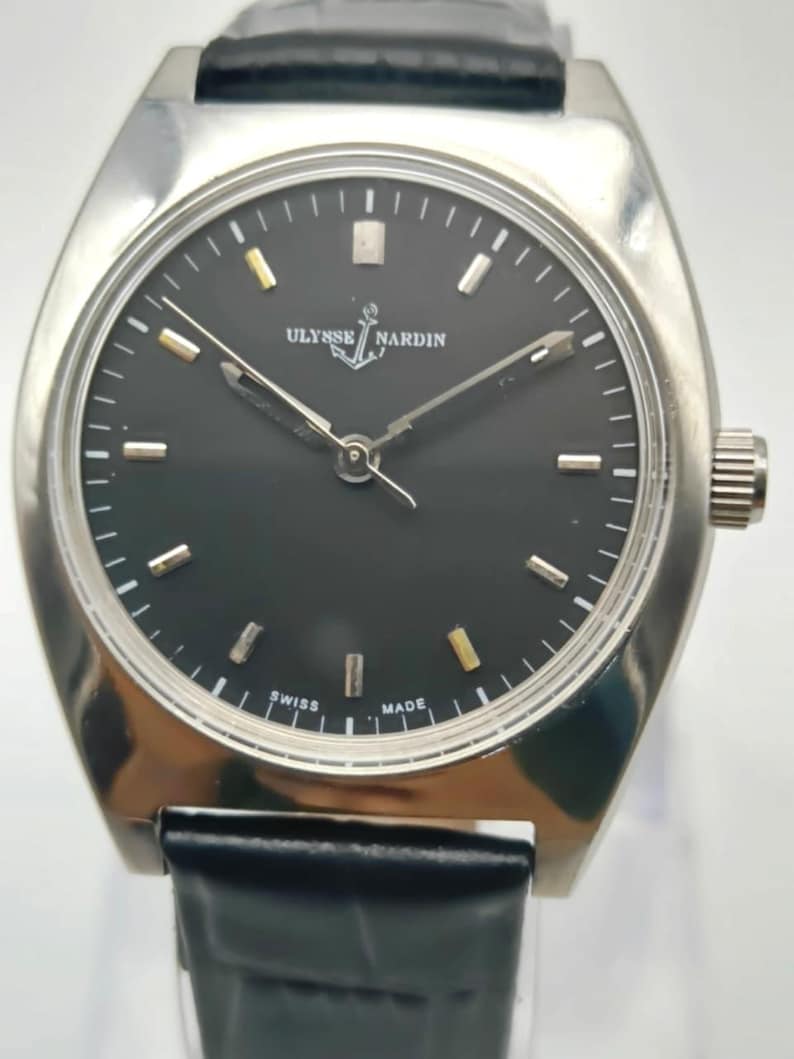 Puede incluir: Un reloj de pulsera Ulysse Nardin plateado con esfera negra y correa de cuero negro. La esfera del reloj tiene marcadores y agujas plateadas y doradas. El reloj est&aacute; marcado "Swiss Made".