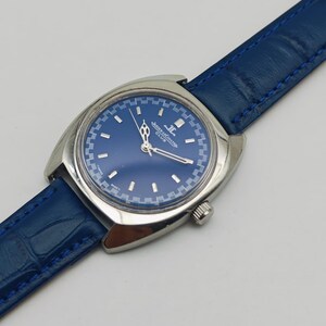 Puede incluir: Un reloj de pulsera vintage con esfera azul y caja plateada. El reloj presenta una correa de cuero azul y el texto "JAEGER-LECOULTRE CLUB" en la esfera. El reloj tiene un dise&ntilde;o cl&aacute;sico.