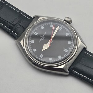 Puede incluir: Un reloj de pulsera de acero inoxidable con esfera negra y correa de cuero negro. La esfera del reloj presenta marcadores de hora y agujas blancas, con un segundero rojo. El reloj est&aacute; marcado "SWISS MADE".