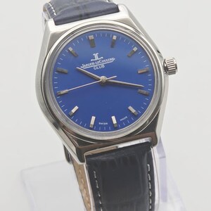 May include: A stainless steel Jaeger-LeCoultre Club watch with a blue dial and black leather strap. The watch features silver hour markers and hands. The text "JAEGER-LECOULTRE CLUB" is printed on the dial. The watch is marked "SWISS MADE".