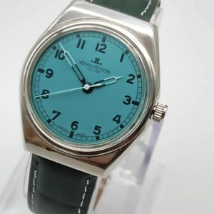 Pode incluir: Um rel&oacute;gio prateado com mostrador turquesa e pulseira de couro verde escuro. O mostrador exibe o logotipo Jaeger-LeCoultre e a palavra "CLUB". A pulseira tem costuras brancas.