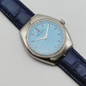 May include: A silver Jaeger-LeCoultre Club watch with a light blue face and a dark blue leather strap. The watch face has silver hands and hour markers. The strap is approximately 20 cm long.