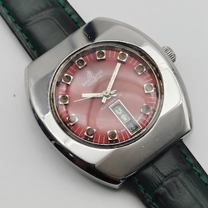 May include: A vintage Breitling Gen&egrave;ve automatic watch with a red dial and a date display. The watch has a silver-tone case and a black leather strap with green stitching. The watch face features silver hands and hour markers.