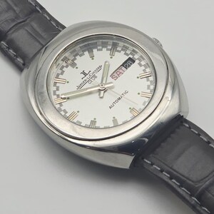 Puede incluir: Un reloj de pulsera autom&aacute;tico Jaeger-LeCoultre Club plateado con esfera blanca. El reloj muestra el d&iacute;a y la fecha, con una correa de cuero negro. La esfera tiene marcadores y agujas doradas. Un reloj cl&aacute;sico.