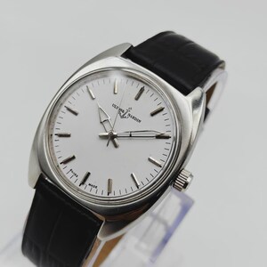 May include: A silver-toned Ulysse Nardin wristwatch with a white face and black leather band. The watch features a round face with silver hour markers and hands. The band is black, and the watch is displayed on a clear stand.