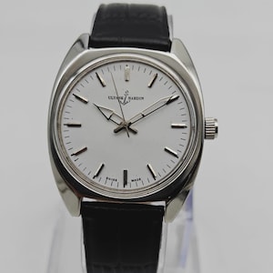 May include: A silver-toned Ulysse Nardin wristwatch with a white face and black leather band. The watch has a round face with silver hands and markers. The watch is displayed on a clear stand.
