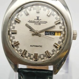 Puede incluir: Un reloj autom&aacute;tico Jaeger-LeCoultre Club vintage con caja plateada y esfera blanca. La esfera muestra el nombre de la marca, d&iacute;a y fecha, y agujas luminosas. El reloj tiene una correa de cuero verde.