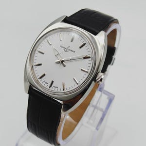 May include: A silver-toned Ulysse Nardin wristwatch with a white face and black leather band. The watch has a round face with silver hands and markers. The band is textured and the watch is displayed on a clear stand.