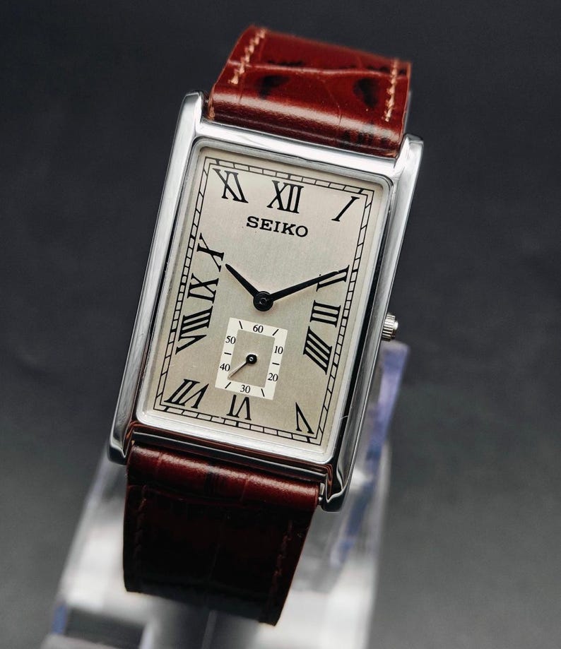 May include: A rectangular Seiko wristwatch with a silver face, black hands, and Roman numeral hour markers. The watch has a brown leather band and a silver case. The watch face includes the word "SEIKO".