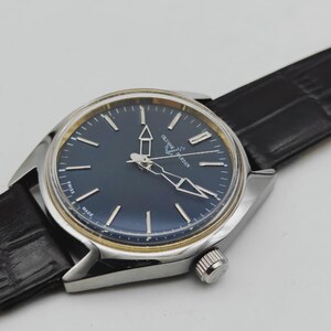 May include: A silver-toned wristwatch with a dark blue face and silver hands and markers. The watch has a black leather band. The watch face has the brand name "Ulysse Nardin" printed on it. The watch is a classic design.