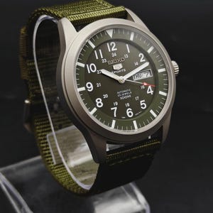 Puede incluir: Un reloj autom&aacute;tico Seiko 5 Sports con caja plateada mate y esfera verde oliva. La esfera presenta n&uacute;meros ar&aacute;bigos blancos, una ventana de d&iacute;a y fecha en la posici&oacute;n de las tres y una correa de tela de nailon verde oliva a juego.