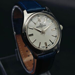 Peut inclure: Une montre Jaeger-LeCoultre Club argent&eacute;e avec un cadran blanc et des aiguilles et index argent&eacute;s. La montre a un bracelet en cuir bleu. Le cadran affiche le logo Jaeger-LeCoultre et les mots "CLUB" et "T SWISS MADE T".