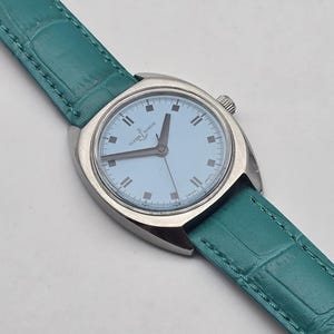 Peut inclure: Une montre-bracelet argent&eacute;e avec un cadran bleu clair et un bracelet en cuir vert d'eau. Le cadran affiche la marque "Ulysse Nardin". Le bracelet a une texture peau de crocodile. Une montre classique.